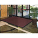 A large burgundy Lavex Chevron Rib entrance mat unrolled in front of a glass door.