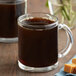 A glass mug filled with brown Caribou Coffee with caramel in it.