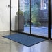 A navy blue Lavex Parquet entrance mat on the floor in front of a glass door.