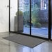 A Lavex gray indoor entrance mat in front of a glass door.