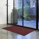 A red Lavex Needle Rib entrance mat on the floor in front of a glass door.