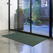 A green Lavex Olefin entrance mat rolled out on the floor in front of a glass door.