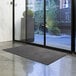 A black Lavex Olefin entrance mat on the floor in front of a glass door.
