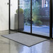 A gray Lavex waffle entrance mat on the floor in front of a glass door.