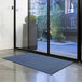 A blue Lavex Olefin entrance mat roll laid out on a floor in front of a glass door.
