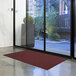A red Lavex Needle Rib entrance mat unrolled on the floor in front of a glass door.