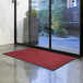 A red Lavex Olefin entrance mat on a floor in front of a glass door.