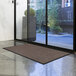 A large brown Lavex Waffle entrance mat on the floor in front of a glass door.