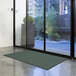 A green Lavex Needle Rib indoor entrance mat roll on the floor in front of a glass door.