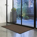 A brown Lavex parquet entrance mat on a floor in front of a glass door.