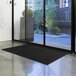 A solid black Lavex Olefin entrance mat on a floor in front of a window.