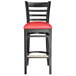 A Lancaster Table & Seating black wood ladder back bar stool with a red vinyl seat.