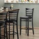A Lancaster Table & Seating black wood ladder back bar stool with a black vinyl seat and back.