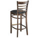 A Lancaster Table & Seating wooden ladder back bar stool with a black vinyl seat.