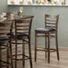 A Lancaster Table & Seating wood ladder back bar stool with a black vinyl seat detached.