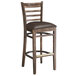 A Lancaster Table & Seating wooden ladder back bar stool with a dark brown vinyl seat on a table in a bar.