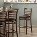 A Lancaster Table & Seating wood ladder back bar stool with a dark brown vinyl seat.