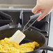 A person using a Linden Sweden white silicone spatula to stir scrambled eggs in a skillet.