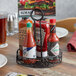 An American Metalcraft wrought iron condiment caddy holding ketchup and hot sauce bottles on a table.