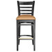 A Lancaster Table & Seating black wood ladder back bar stool with light brown cushion.