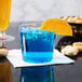 A close up of a WNA Comet Classicware clear plastic fluted tumbler filled with a blue drink and an orange slice.