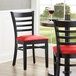A Lancaster Table & Seating black wood ladder back chair with a red vinyl seat.