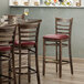 A Lancaster Table & Seating wood ladder back bar stool with a burgundy vinyl seat on a table in a restaurant.