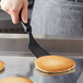A hand holding a black Linden Sweden Gourmaid spatula over a pancake cooking on a pan.