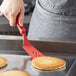 A person using a red Linden Sweden Gourmaid silicone spatula to flip a pancake.