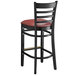 A black Lancaster Table & Seating wood bar stool with a burgundy cushioned seat and ladder back.