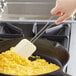 A white Linden Sweden silicone spatula with a stainless steel handle stirring scrambled eggs in a pan.