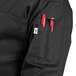 A close up of a person wearing a black Uncommon Chef long sleeve chef coat with a tool in the pocket.