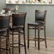 A Lancaster Table & Seating Sofia wood bar stool with a black vinyl seat.