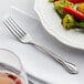 An Acopa stainless steel dinner fork on a white plate with vegetables.