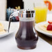 A Tablecraft syrup dispenser filled with syrup on a table next to a plate of pancakes.