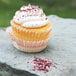 A cupcake with white frosting and sprinkles on a rock.
