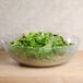A Cambro pebbled serving bowl filled with green salad on a table.
