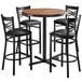A Lancaster Table & Seating round bar table with butcher block top and 4 black chairs around it.