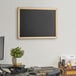 A Dynamic by 360 Office Furniture black wall-mounted chalkboard with a wood frame.