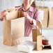 A woman opening a brown paper bag to reveal a white box with a lid inside.