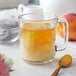 A glass mug of Bossen Peach Oolong tea with a peach on the rim and a spoon.