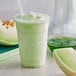 A close-up of a green honeydew smoothie in a plastic cup.