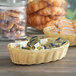 A Vollrath natural-colored plastic rattan bread basket filled with pastries on a hotel buffet counter.
