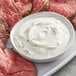 A plate of sliced steak with a bowl of white horseradish sauce.