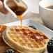 A person pouring sugar free pancake syrup on a waffle.