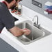 A man washing his hands in a Regency stainless steel drop-in sink with gooseneck faucet on a counter.