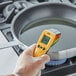 A hand holding a yellow and black CDN Infrared Thermometer over a pot of boiling water.
