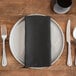 A plate with a Snap Drape charcoal cloth napkin and silverware on a wooden table.
