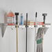 A Regency stainless steel utility shelf with mop and broom holders and rag hooks holding cleaning supplies and tools.