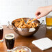 A hand holding a Vollrath stainless steel bowl of pretzels over a glass of beer.